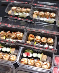 a variety of sushi in plastic containers lined up on a table