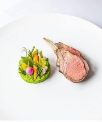 a plate of lamb and vegetables on a white plate